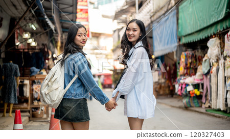 Two pretty Asian female friends hold hands and smiles at the camera, explore the city together. Two pretty Asian female friends hold hands and smiles at the camera, explore the city together. 120327403
