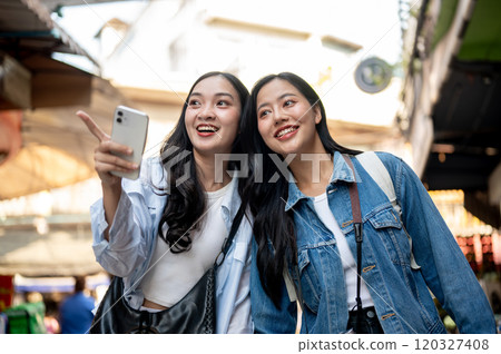 Two pretty, excited Asian women enjoy exploring a local market in a Southeast Asian city together. 120327408