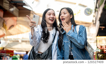 Two pretty, excited Asian women enjoy exploring a local market in a Southeast Asian city together. 120327409