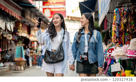 Two happy Asian female tourists explore a local market in Thailand, walking along the street. Two happy Asian female tourists explore a local market in Thailand, walking along the street. 120327416