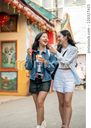 Two joyful Asian female friends explore the city in Chiang Mai, Thailand, enjoying ice cream. 120327425