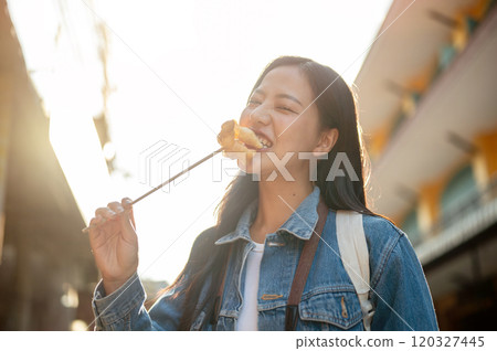 A joyful Asian woman enjoys Thailand's street food while strolling through the city on a sunny day. A joyful Asian woman enjoys Thailand's street food while strolling through the city on a sunny day. 120327445