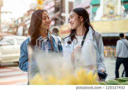Two cheerful, cute Asian female tourists buy street food in Thailand. 120327492