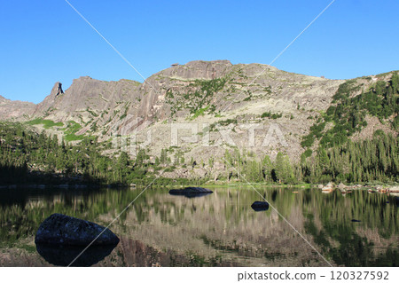 Lake with regrowth in mountains, green forest, high cliffs at sunset, blue sky Lake with regrowth in mountains, green forest, high cliffs at sunset, blue sky 120327592
