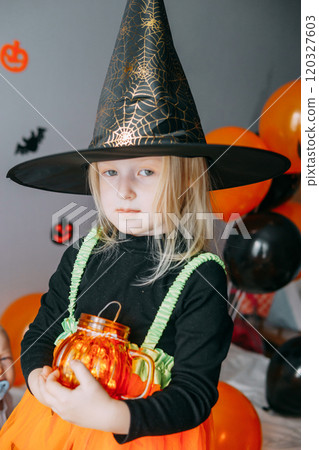 Children's Halloween - a girl in a witch hat and a carnival costume with airy orange and black balloons at home. Ready to celebrate Halloween 120327603