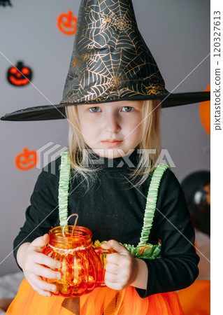 Children's Halloween - a girl in a witch hat and a carnival costume with airy orange and black balloons at home. Ready to celebrate Halloween Children's Halloween - a girl in a witch hat and a carnival costume with airy orange and black balloons at home. Ready to celebrate Halloween 120327613