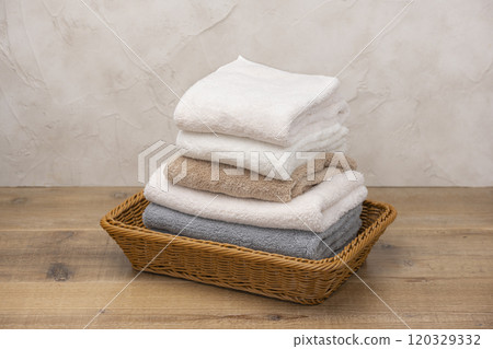 Folded and stacked towels in a basket in front of a white wall Folded and stacked towels in a basket in front of a white wall 120329332