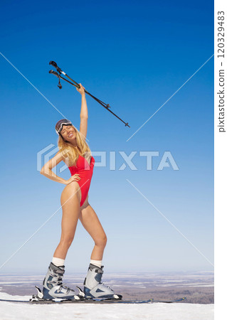 Attractive happy woman model in red swimsuit with skis on ski slope. 120329483