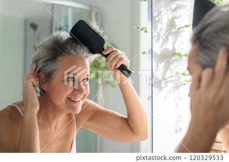 European beautiful and smiling middle-aged woman combing her gray hair 120329533