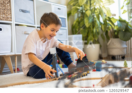 A small white-skinned European boy builds a toy railway at home on the carpet. The child play 120329547