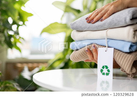 Woman holds a stack of knitwear. Recyclable product concept. Label with recycling icon Woman holds a stack of knitwear. Recyclable product concept. Label with recycling icon 120329628