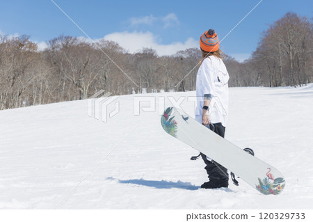 一個年輕女子站在斜坡上，拿著滑雪板，滑雪板圖像 120329733