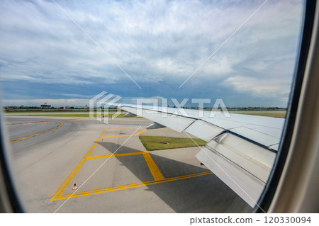 Through the airplane window, Suvarnabhumi International Airport comes into view, along with the expansive wings of the aircraft, amid the midday hustle. 120330094