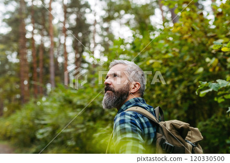 Handsome man standing in the middle of nature, enjoying peaceful atmosphere of the forest, forestbathing. 120330500