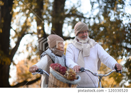 Elderly couple on walk in park, pushing their bikes side by side. Seniors in love on stroll through autumn city, enjoying a peaceful moment together. 120330520