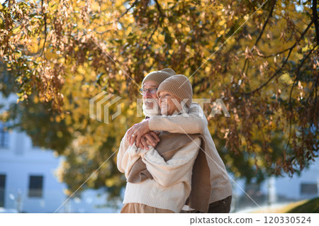 Portrait of beautiful senior couple during walk in autumn park. Elderly husband and wife are embracing each other. 120330524