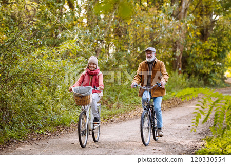 Beautiful elderly couple on bike ride in the forest. Seniors in love cycling through autumn nature, enjoying a peaceful moment. 120330554