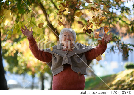 Portrait of elderly woman on walk in the park enjoying warm autumn day, throwing colorful leaves. Portrait of elderly woman on walk in the park enjoying warm autumn day, throwing colorful leaves. 120330578