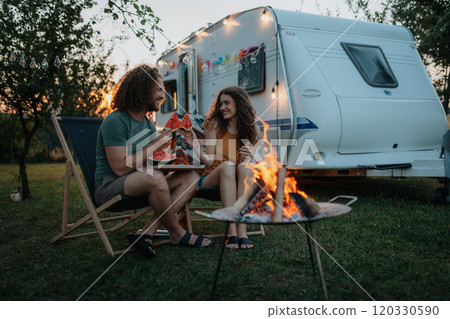Couple having romantic picnic during camping trip in nature, eating watermelon. Caravan traveling for young people. Couple having romantic picnic during camping trip in nature, eating watermelon. Caravan traveling for young people. 120330590
