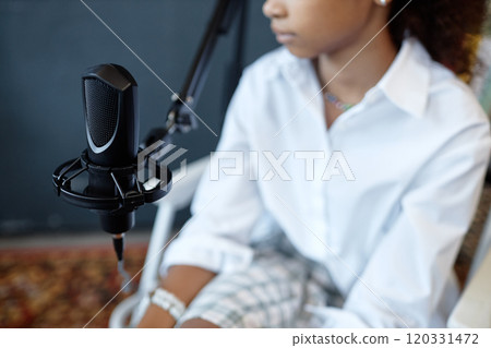 Side view close up of studio microphone on stand with African American girl speaking and recording podcast, copy space 120331472