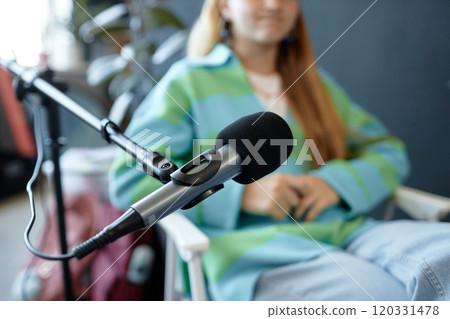 Close up of professional studio microphone on stand with unrecognizable teenage girl speaking in defocused background and recording podcast 120331478