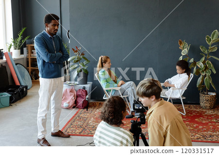 Backstage shot of group of teenage children setting up studio for recording podcast or video together with teacher helping, copy space Backstage shot of group of teenage children setting up studio for recording podcast or video together with teacher helping, copy space 120331517
