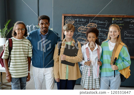 Diverse group of young children posing together standing in school classroom and smiling at camera with male teacher Diverse group of young children posing together standing in school classroom and smiling at camera with male teacher 120331647
