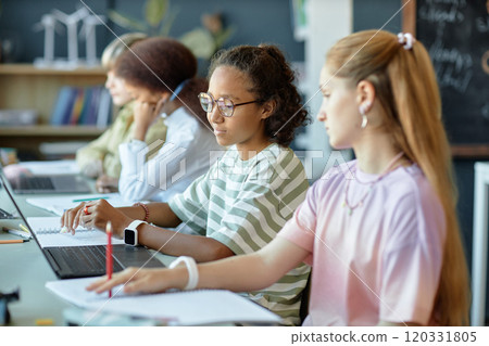 Side view of diverse group of children sitting in row in school classroom and using computer 120331805