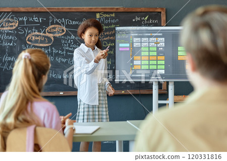 Portrait of young African American girl giving presentation on IT and programming to group of children in school classroom standing by blackboard Portrait of young African American girl giving presentation on IT and programming to group of children in school classroom standing by blackboard 120331816