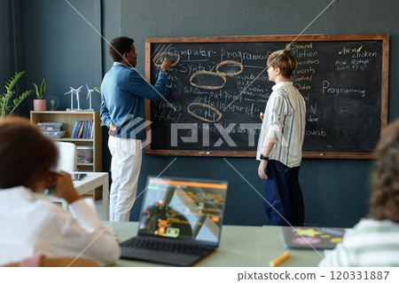 Scene of school classroom with male teacher and student writing on blackboard together learning programming and software development 120331887