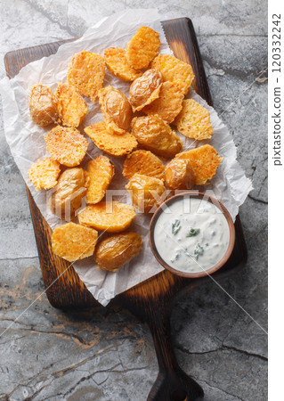 Crispy Roasted Parmesan Potatoes served with sour cream sauce close up on the wooden board. Vertical top view Crispy Roasted Parmesan Potatoes served with sour cream sauce close up on the wooden board. Vertical top view 120332242