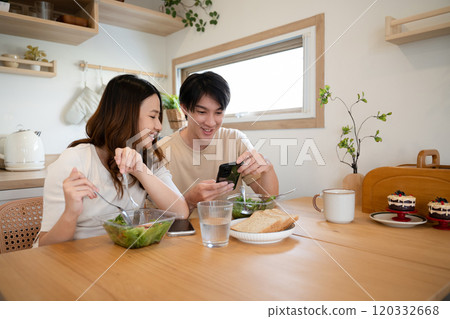 Smiling couple enjoying fresh salad and using mobile phone in a cozy kitchen Smiling couple enjoying fresh salad and using mobile phone in a cozy kitchen 120332668