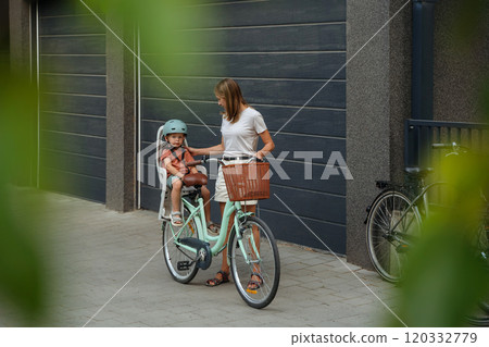 Child with helmet seats in rear bicycle child seat, ready for ride with his mom 120332779