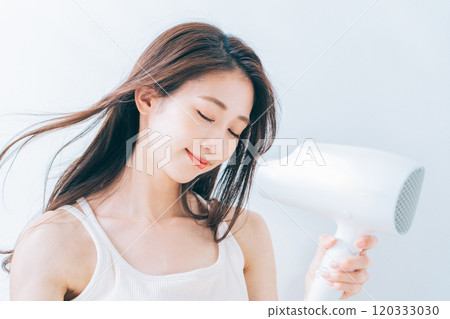 婦女用吹風機烘乾她的頭髮。 120333030