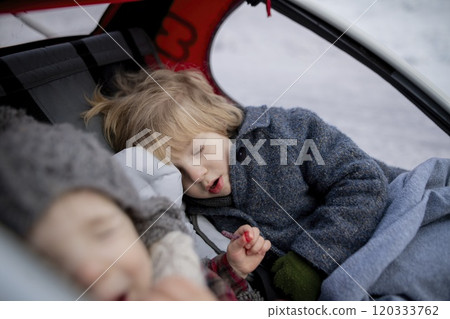 Winter holiday in the mountains. Sibligns sleeping in wagon stroller during walk in snowy forest. 120333762