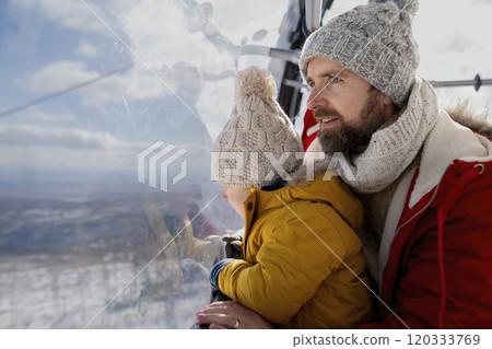 Father and young son on a winter holiday is riding cable car to the top of the mountain. Father and young son on a winter holiday is riding cable car to the top of the mountain. 120333769
