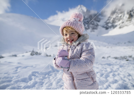 Portrait of small girl enjoying winter holiday in the mountains with family, playing in snow. 120333785