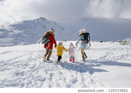 Young family is enjoying winter holiday in the mountains, holding hands while walking through the snowy landscape. 120333802