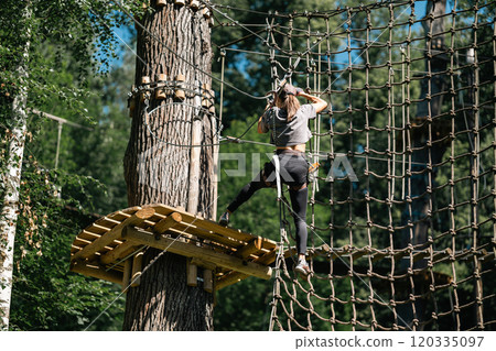 A person skillfully navigating a ropes course situated high among the trees, showcasing both thrill and adventure A person skillfully navigating a ropes course situated high among the trees, showcasing both thrill and adventure 120335097
