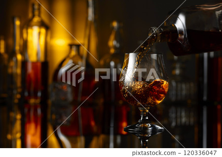 Pouring brandy from a bottle into a glass. Pouring brandy from a bottle into a glass. 120336047