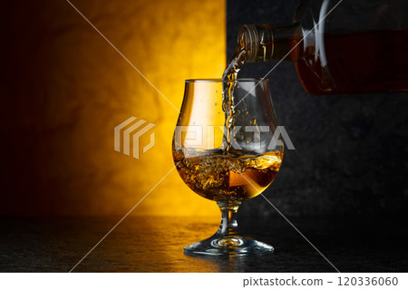 Pouring brandy from a bottle into a glass. Pouring brandy from a bottle into a glass. 120336060