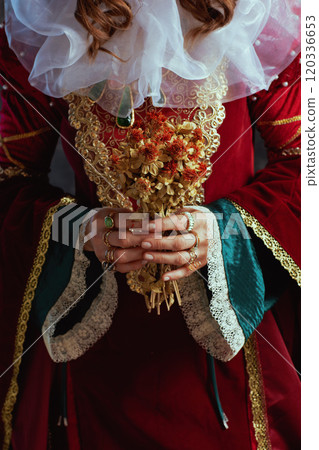 Closeup on medieval queen in red dress with dried flower Closeup on medieval queen in red dress with dried flower 120336653