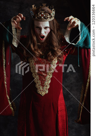scary medieval queen in red dress with white makeup and crown 120336664