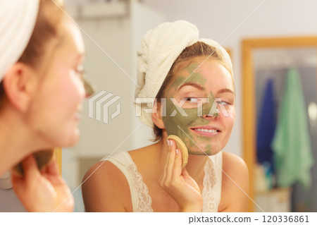 Woman removing facial clay mud mask in bathroom 120336861