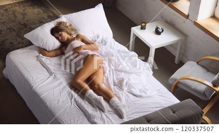 aerial view of woman wearing light pink sleepwear outfit and white socks, with natural light coming through window. 120337507