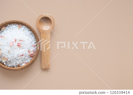 Wooden bowl filled with bath salts and petals with wooden spoon on beige background. Wooden bowl filled with bath salts and petals with wooden spoon on beige background. 120339414