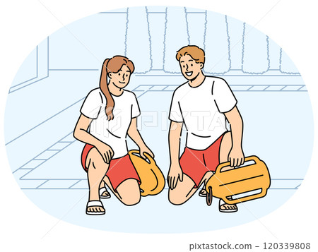 Pair of lifeguards sit by pool at hotel, holding swim training aids and keeping visitors safe 120339808