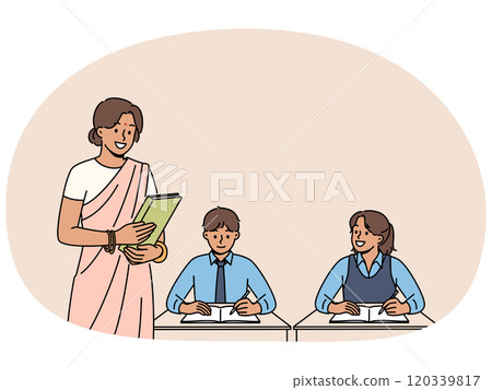 Indian woman teacher works in primary school, standing near children sitting at desks in classroom Indian woman teacher works in primary school, standing near children sitting at desks in classroom 120339817