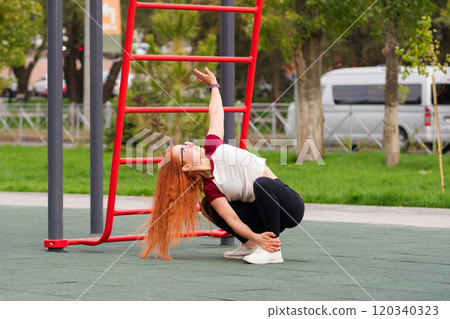 Woman stretching upward while squatting during outdoor exercise 120340323