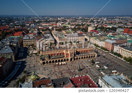 Aerial view of Krakow main market square with historic Cloth Hall (Sukiennice) surrounding colorful buildings on sunny day. Cityscape of Krakow in Poland with tourists walking in old town Aerial view of Krakow main market square with historic Cloth Hall (Sukiennice) surrounding colorful buildings on sunny day. Cityscape of Krakow in Poland with tourists walking in old town 120340427